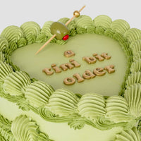 The Olive Martini Heart Cake by Jenna Rae Cakes features a heart-shaped green cake with piped frosting, gold a tini bit older lettering, and a cocktail olive on a toothpick.