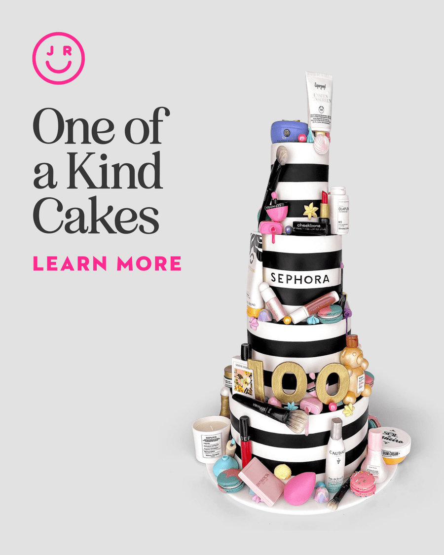 A tiered cake adorned with makeup and skincare in Sephora packaging, plus brushes and cosmetics. Text: One-of-a-Kind Cakes by Jenna Rae Cakes. Learn More. Smiling face logo in top left corner.