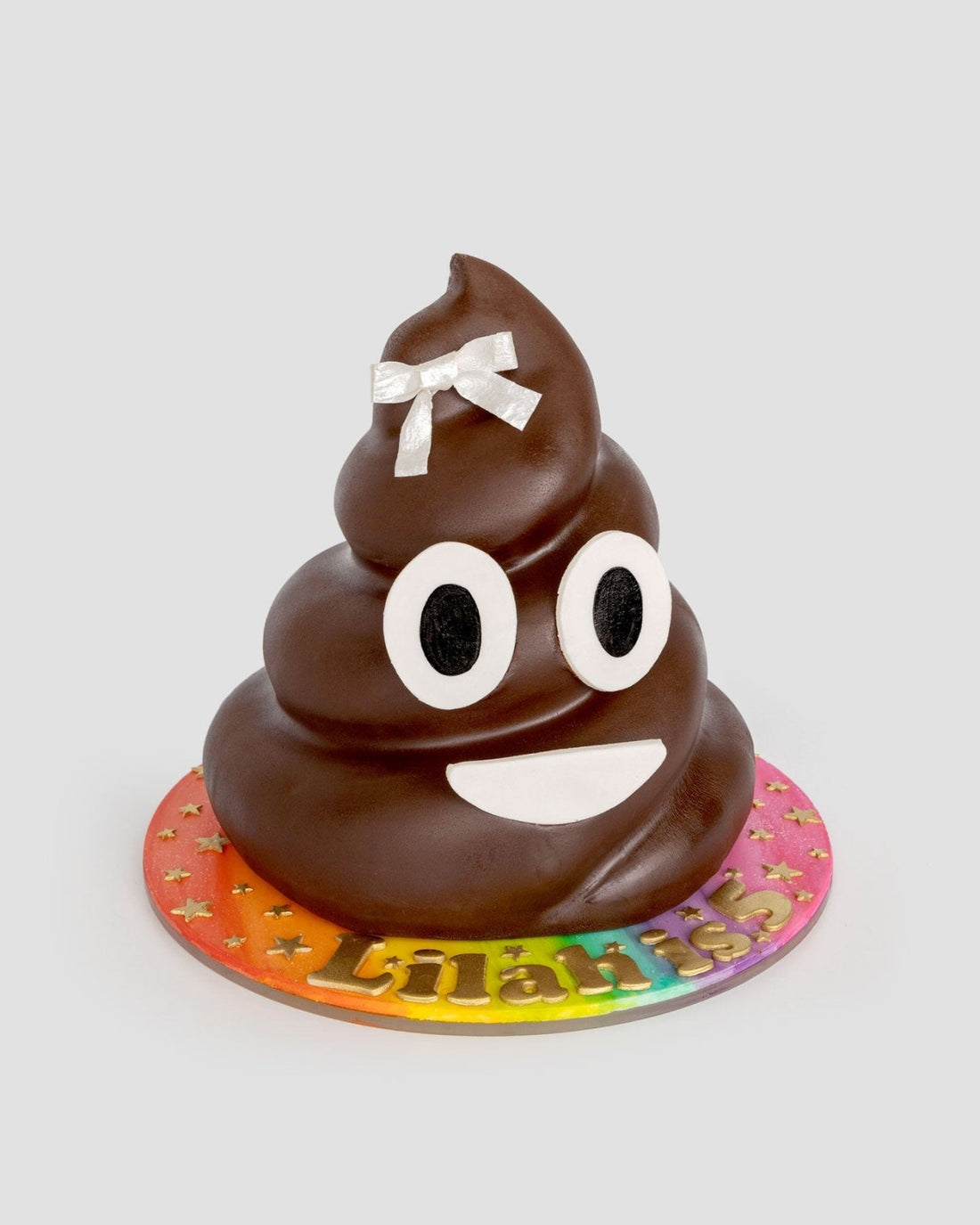 The One-of-a-Kind Cakes by Jenna Rae Cakes features a poop emoji shape with big eyes, a wide smile, and a white bow on top, set on a colorful star-patterned base personalized with the name “Lilani.”.