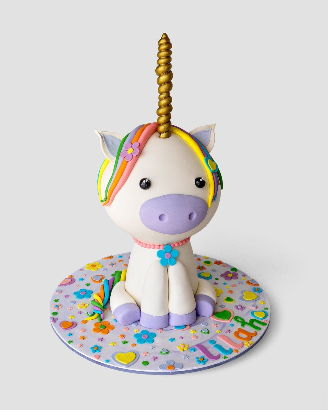 The One-of-a-Kind Cakes by Jenna Rae Cakes features a unicorn cake with a golden horn, rainbow mane, purple accents, and a decorated base with flowers, hearts, and LILIANO in vibrant letters.