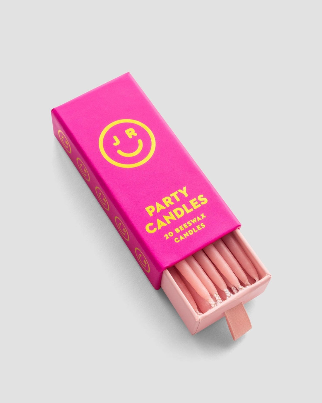 A partially open pink box labeled Party Candles by Jenna Rae Cakes with yellow text and smiley face graphics reveals several pink beeswax candles inside.