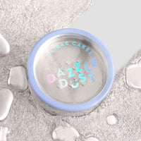 A round container of Jenna Rae Cakes Pearl Edible Lustre Dust (5g Shaker, Pack of 6) with a blue rim and holographic label rests on a silver textured surface, surrounded by droplets. The container holds shimmering edible powder.