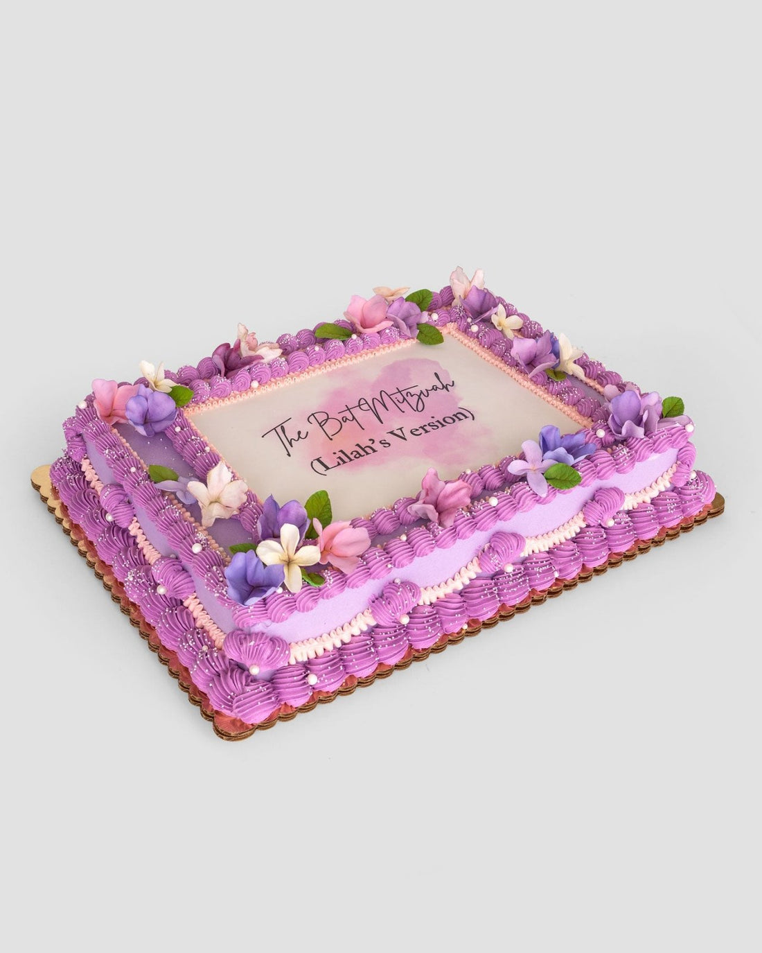 The Sugar Flower Sheet Cake by Jenna Rae Cakes is a rectangular cake with purple icing, pink and purple flowers, green leaves, and “The Past is Prologue (Gladia’s Version)” written in the center.