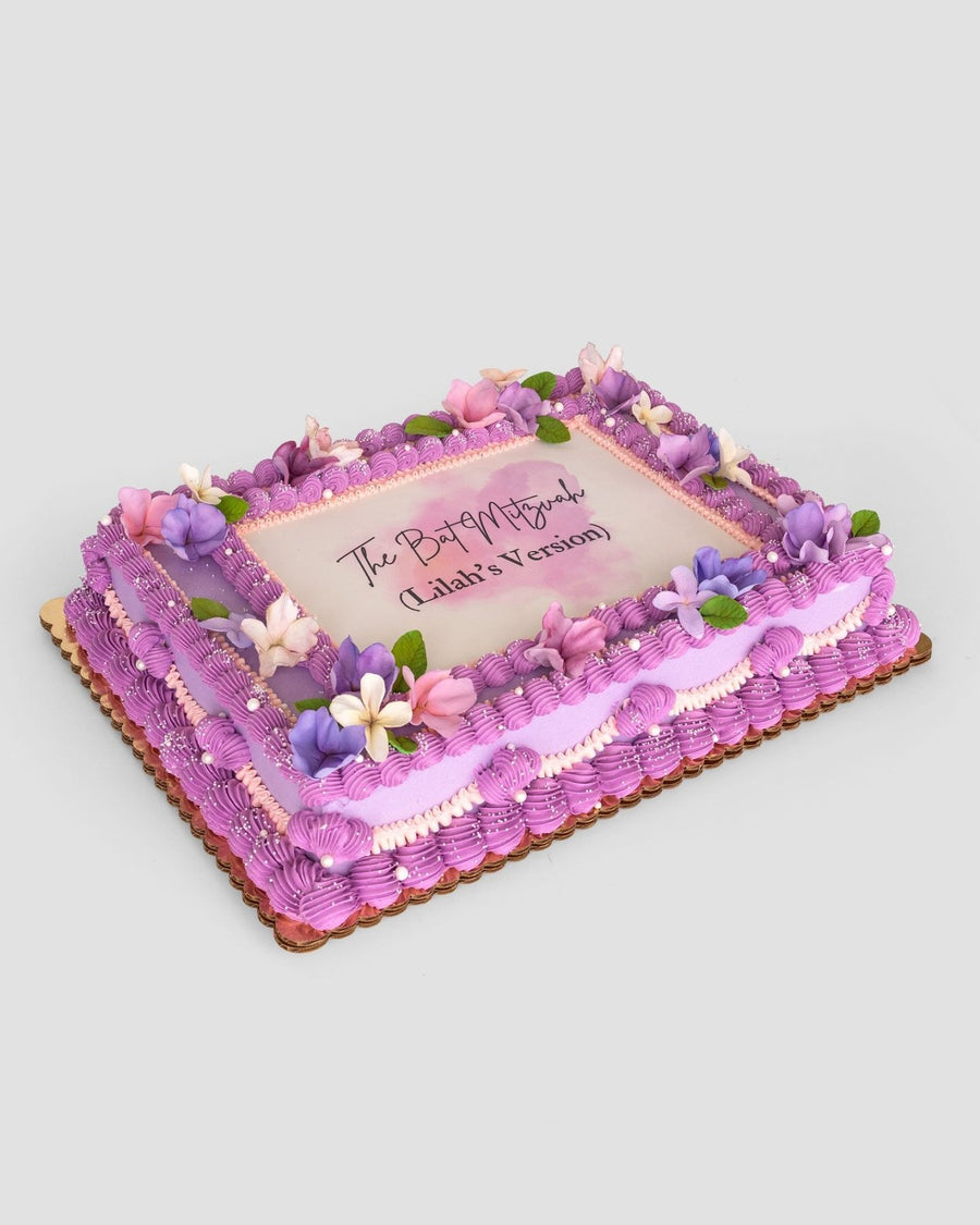 The Sugar Flower Sheet Cake by Jenna Rae Cakes is a rectangular cake with purple icing, pink and purple flowers, green leaves, and “The Past is Prologue (Gladia’s Version)” written in the center.