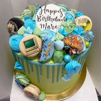The Full Works Cake by Jenna Rae Cakes is a round birthday cake with blue and green icing, meringues, macarons, edible images of a computer and DVD, plus a white Happy Birthday Marc topper.