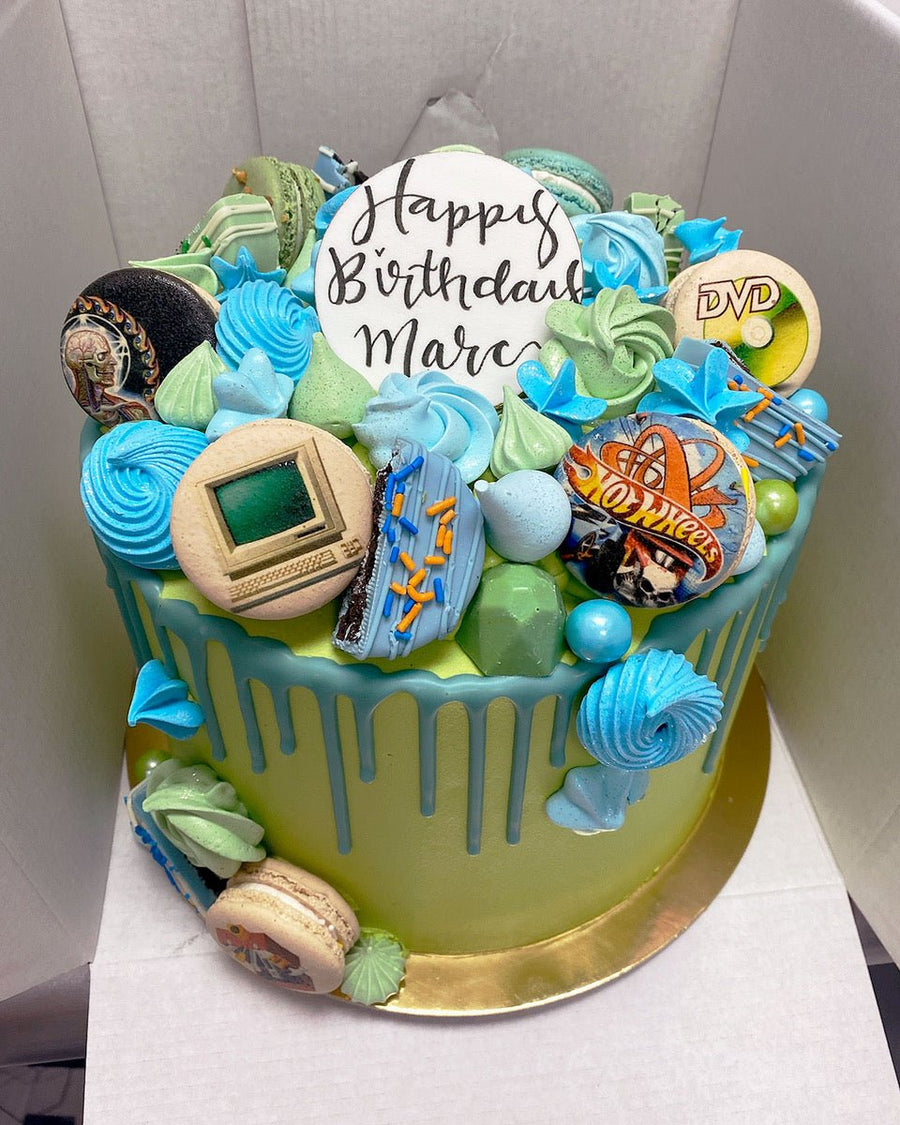 The Full Works Cake by Jenna Rae Cakes is a round birthday cake with blue and green icing, meringues, macarons, edible images of a computer and DVD, plus a white Happy Birthday Marc topper.