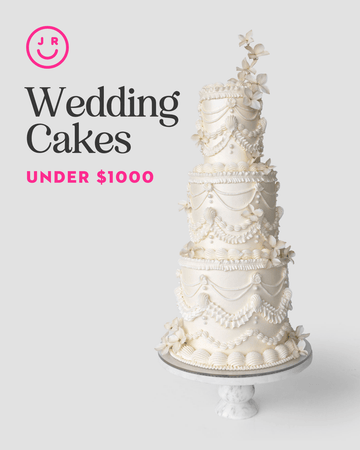 A tall, white multi-tiered wedding cake with icing garlands and sugar flowers sits on a marble stand. Jenna Rae Cakes’ Wedding Cakes Under $1,000. Pink smiley logo above.