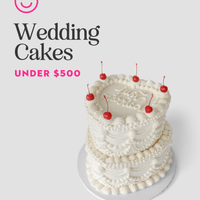 A three-tiered white wedding cake from Jenna Rae Cakes, decorated with cherries, sits on a white surface. On the left, text reads “Wedding Cakes Under $500” with a pink smiley face logo above.