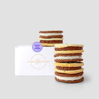 A stack of cookie sandwiches from the Jenna Rae Cakes Cookie Sandwich Gift Box is displayed in front of a white box on a light grey background.