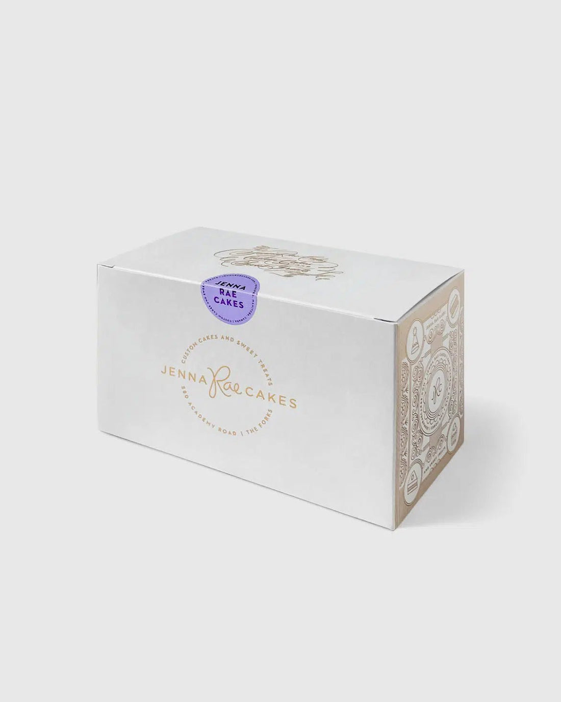 A white rectangular Cookie Sandwich Gift Box from Jenna Rae Cakes, featuring a gold logo on the front, decorative side patterns, and a purple Baked Cakes sticker on top.