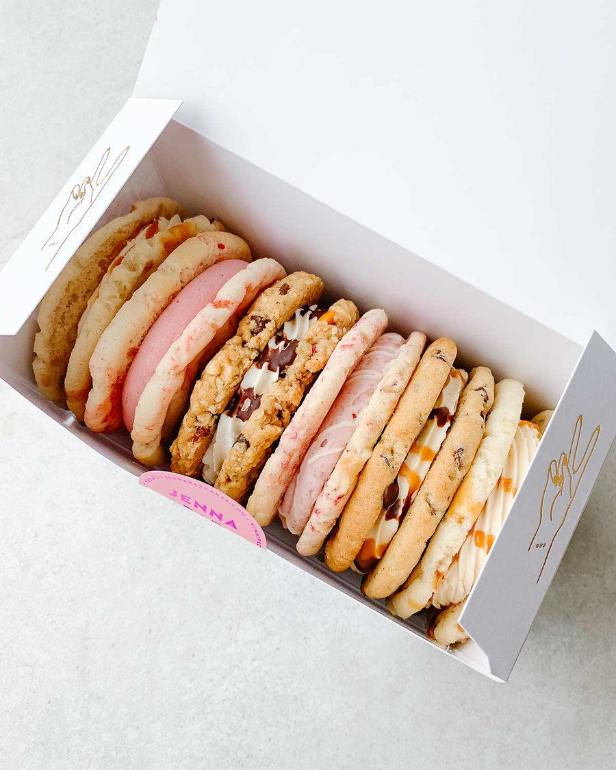 The Cookie Sandwich Gift Box by Jenna Rae Cakes features six large, assorted cookies in different flavors and colors, neatly arranged in a white box on a light background.