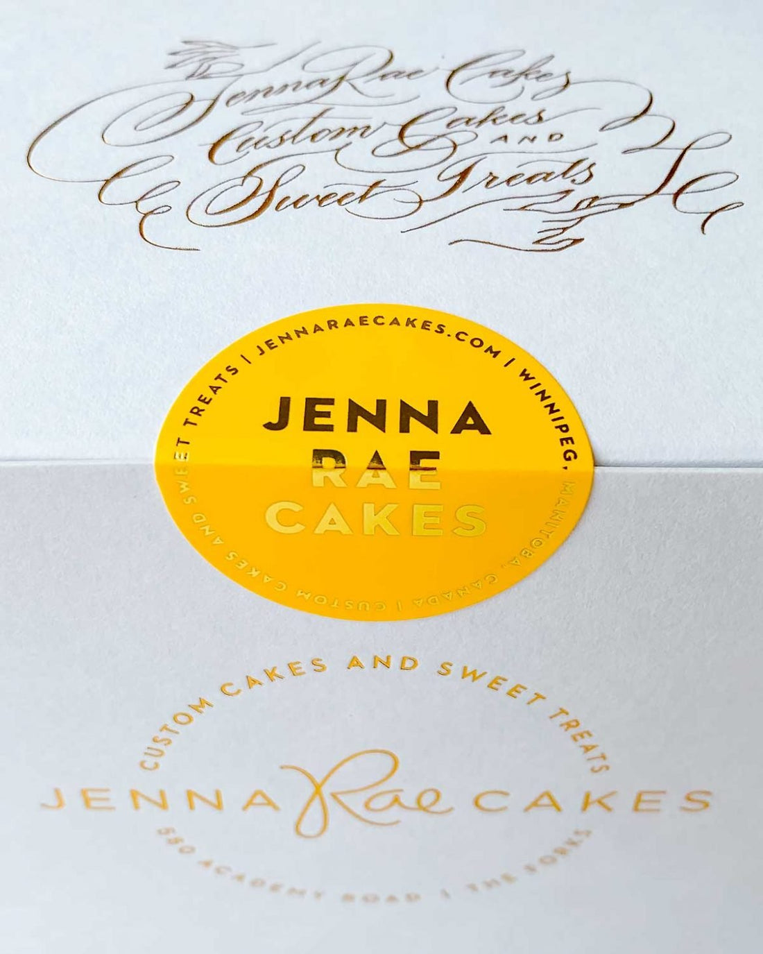 A white box labeled “Cookie Sandwich Gift Box” from Jenna Rae Cakes, featuring elegant script and a round yellow sticker with branding and website details.