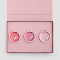 The Jenna Rae Cakes Dazzle Dust Box is an open pink box with “MAKE LIFE DAZZLE” inside the lid, holding three round “Dazzle Dust” makeup containers in varying pink shades.