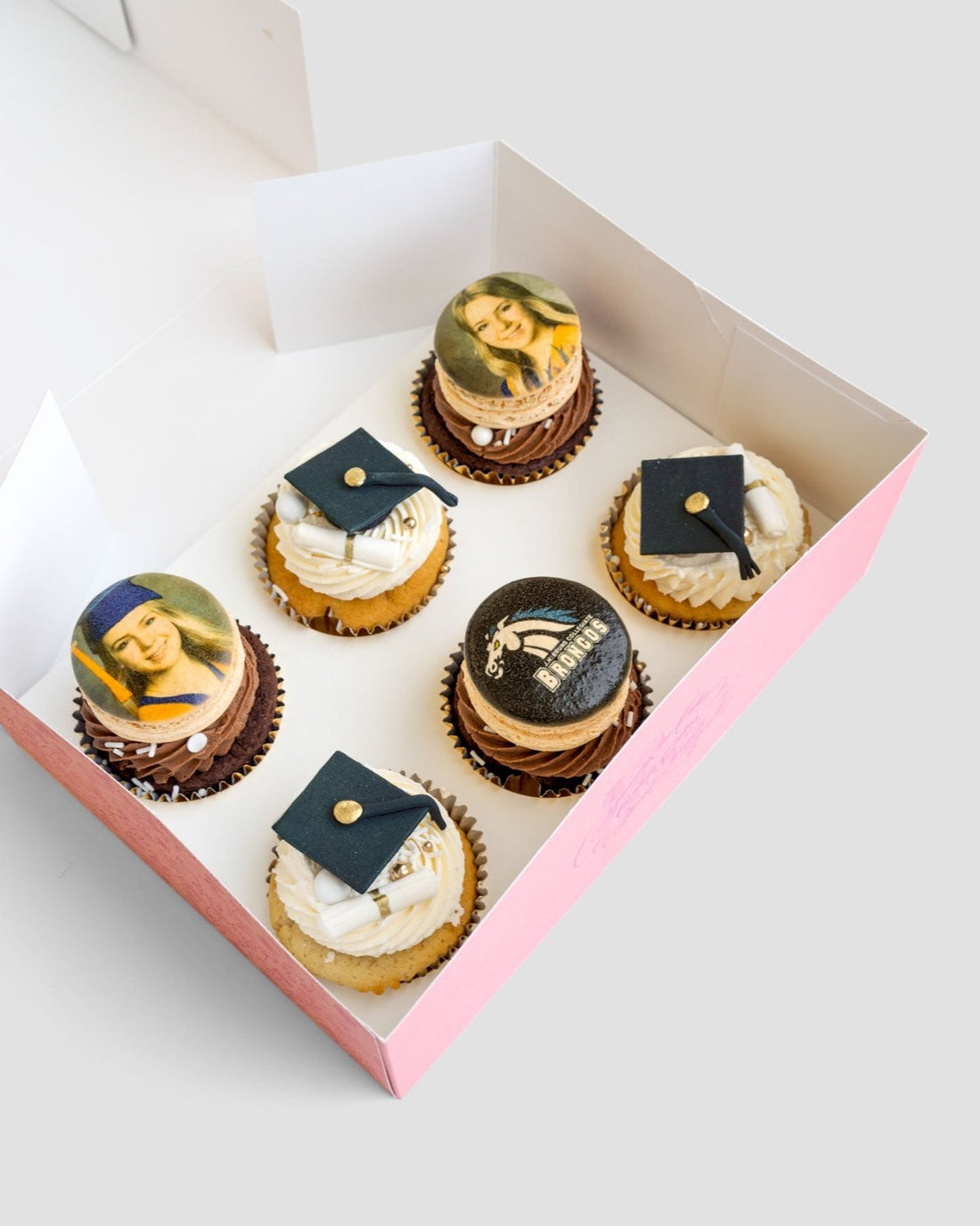 Jenna Rae Cakes Grad Works Cupcakes come in a pink box of six: three topped with edible famous painting images, and three decorated with black graduation caps and diplomas on white frosting.