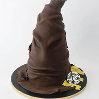 A cake shaped like the Harry Potter Sorting Hat, with detailed brown folds and a “Happy Birthday Mike” sign on a yellow and black scarf at the base.