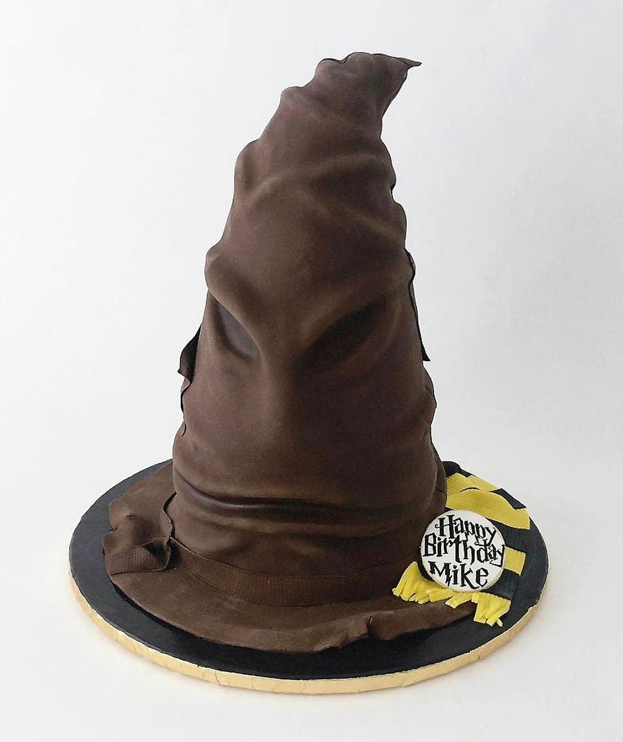 A cake shaped like the Harry Potter Sorting Hat, with detailed brown folds and a “Happy Birthday Mike” sign on a yellow and black scarf at the base.