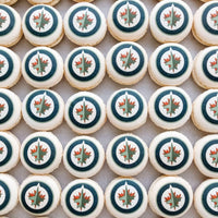 A grid of Printed Macarons by Jenna Rae Cakes, each topped with the Winnipeg Jets logo featuring a red maple leaf and jet in a blue and white circle.