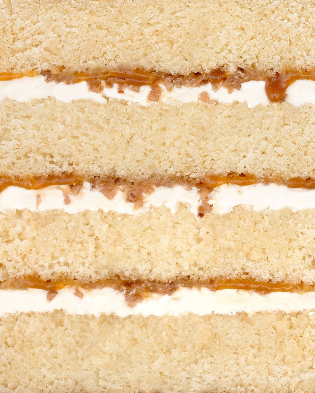 Close-up of Salted Caramel Crunch Cake by Jenna Rae Cakes, featuring layers of light yellow sponge, white cream filling, and a thin layer of caramel between the layers. The image highlights the cake’s texture and detail.