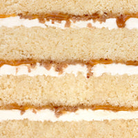 Close-up of Salted Caramel Crunch Cake by Jenna Rae Cakes, featuring layers of light yellow sponge, white cream filling, and a thin layer of caramel between the layers. The image highlights the cake’s texture and detail.