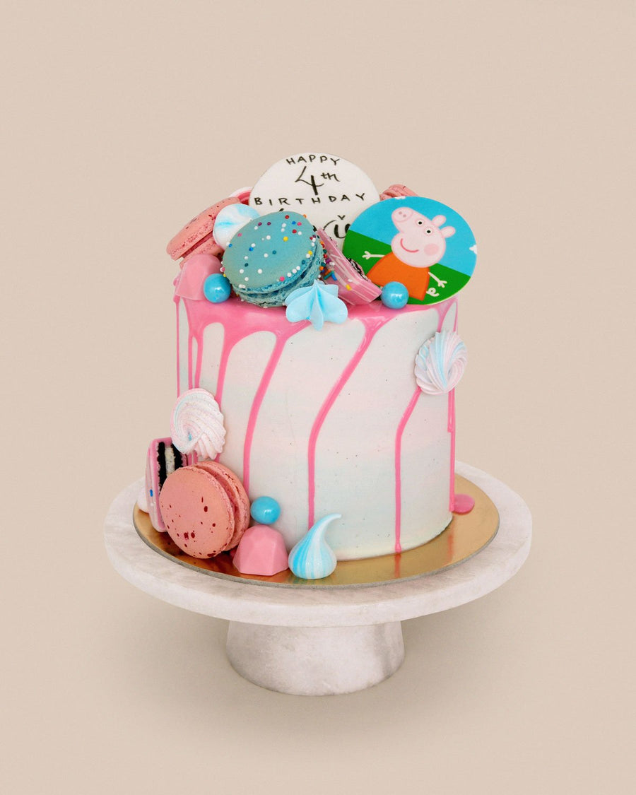 The Kids Works Cake by Jenna Rae Cakes features pink icing drips, colorful macarons, meringues, blue candies, and a Peppa Pig topper on a marble stand. A white “Happy 4th Birthday” topper completes the look against a beige background.