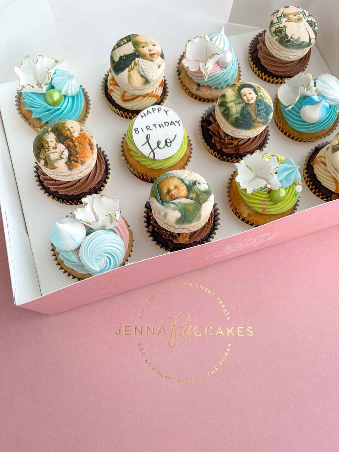 A box of The Works Cupcakes by Jenna Rae Cakes features pastel swirls, edible classical painting images, and white chocolate toppers. One cupcake says Happy Birthday Leo, all presented in a signature pink Jenna Rae Cakes box.