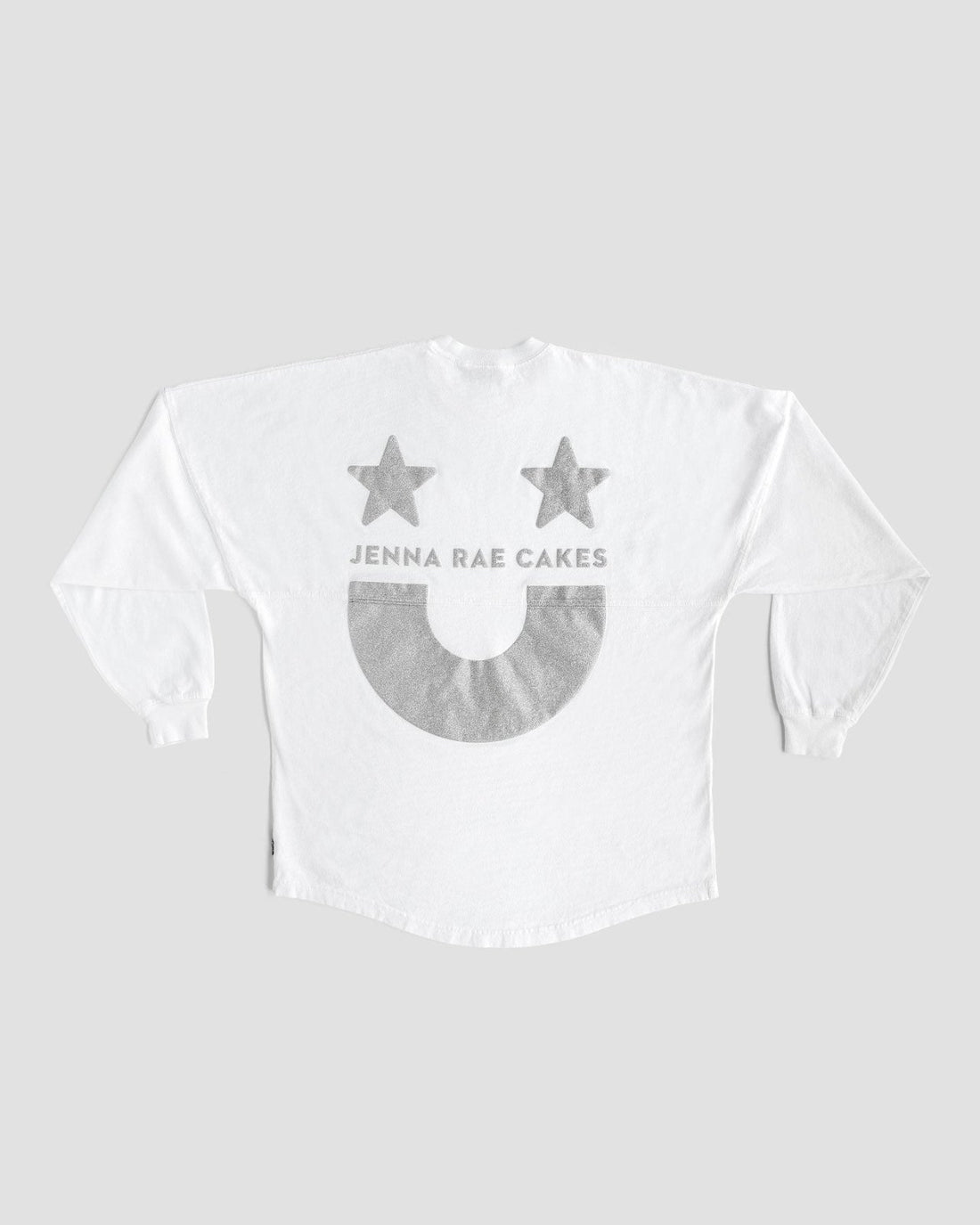 The White and Silver Spirit Jersey by Jenna Rae Cakes features two gray stars, “JENNA RAE CAKES” text, and a large gray smiley face on the back, shown on a plain gray background.