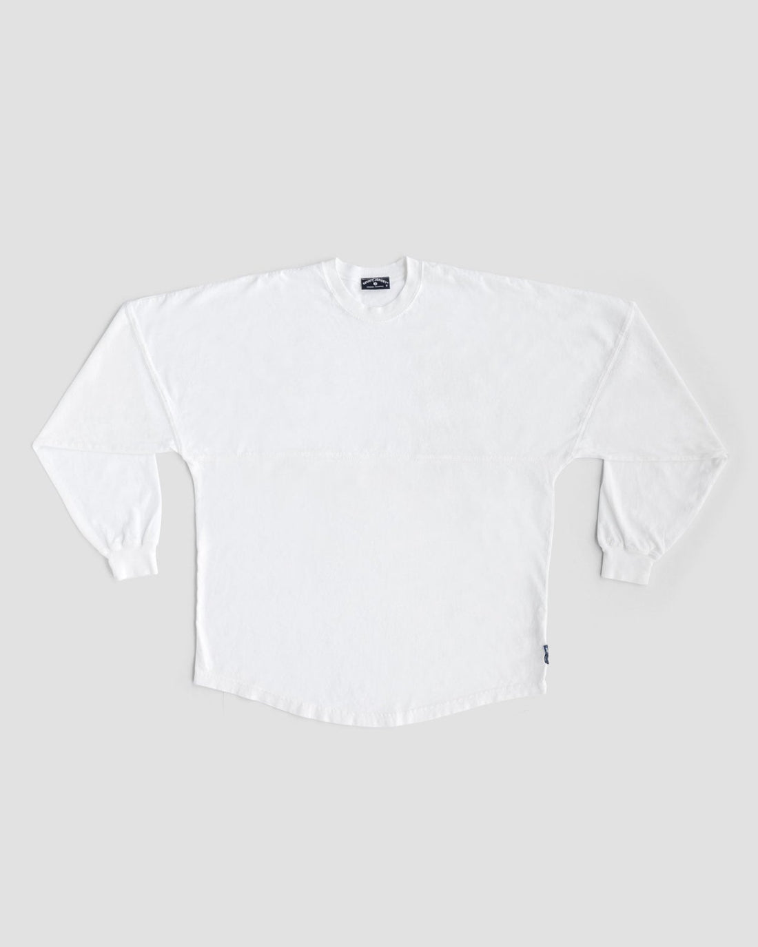 A Jenna Rae Cakes White and Silver Spirit Jersey is laid flat on a light gray background, featuring long sleeves, ribbed cuffs, and a small dark tag on the lower side seam. No visible patterns or logos are present.